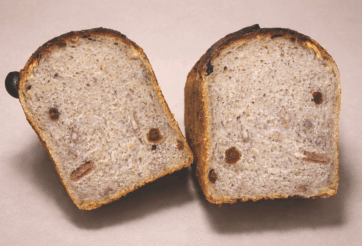 Sezioni di pane Nociatino artigianale. Pane con noci e uvetta, crosta dorata. Perfetto per colazione o snack.