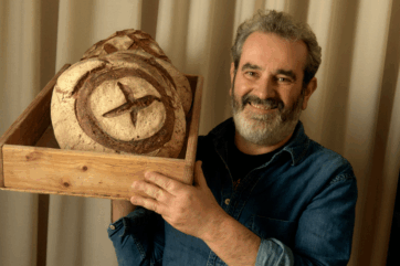 Davide Longoni con pane a lievitazione naturale. Panettiere sorridente con pane artigianale in cassetta di legno.