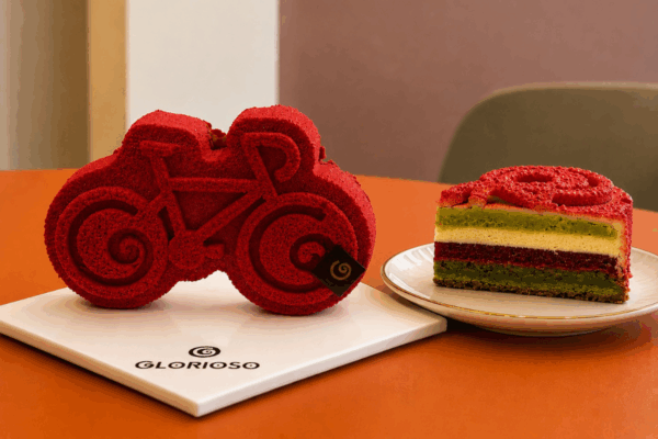 Torta Emilio Glorioso a forma di bici rossa. Pasticceria artigianale e fetta di torta.
