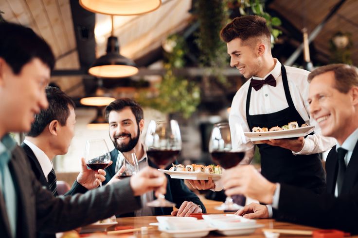 Giornata della Ristorazione: cameriere serve sushi e vino rosso a clienti sorridenti in un ristorante elegante.