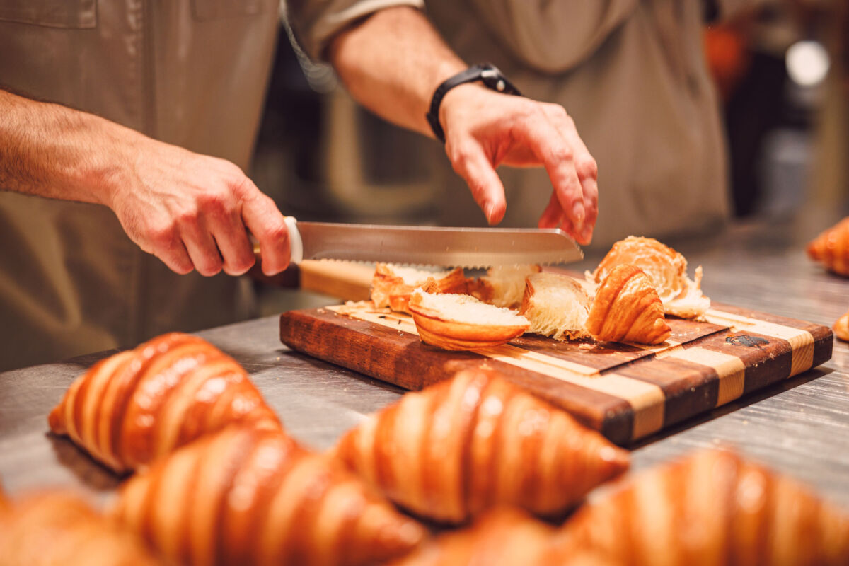 Mani di un professionista tagliano croissant artigianali su un tagliere in legno per l'evento 360 Grani di Molino Mariani.