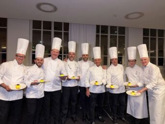 Gruppo di pasticceri AMPI in divisa presenta il dolce Lumen creato per la Fondazione Telethon durante un evento.
