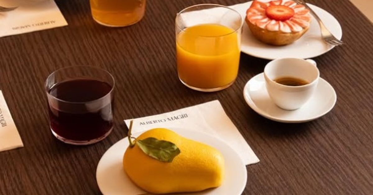 Colazione gourmet all'atelier del dolce Alberto Magrì: pasticceria, succhi e caffè su tavola in legno a Milano.