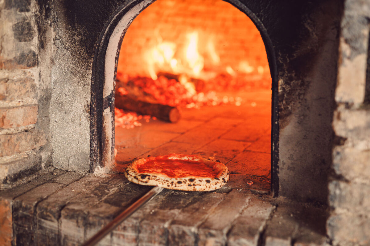 Pizza in cottura nel forno a legna: l'Arte Bianca di Molino Paolo Mariani e 360 Grani con fiamme vive e fuoco ardente.