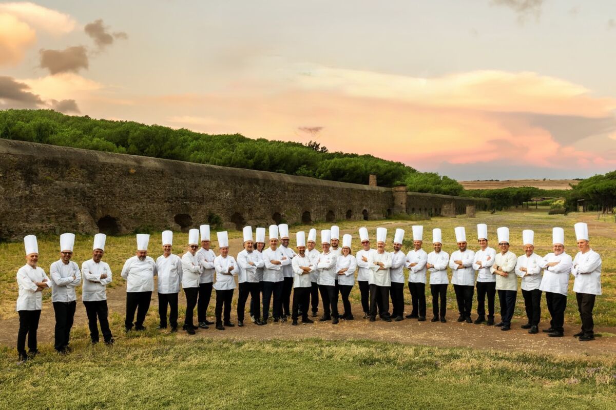 Gruppo di pasticceri FIPGC in divisa al Simposio Tecnico di Roma davanti all'antico acquedotto al tramonto.