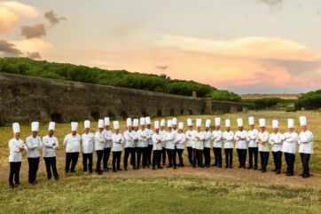 Gruppo di pasticceri FIPGC in divisa al Simposio Tecnico di Roma davanti all'antico acquedotto al tramonto.