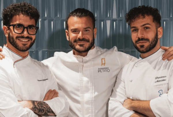 Alessandro Petito e il suo team di pasticceri professionisti in divisa bianca su sfondo blu, maestri della pasticceria.