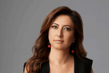 Ritratto di Cristina Scocchia, Amministratore Delegato di illycaffè, con capelli castani e orecchini rossi su sfondo grigio.