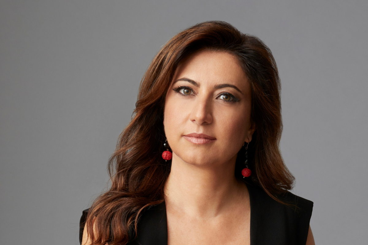 Ritratto di Cristina Scocchia, Amministratore Delegato di illycaffè, con capelli castani e orecchini rossi su sfondo grigio.