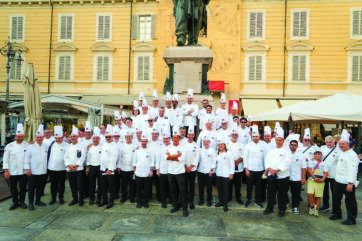 Gruppo di chef in divisa bianca posa per la Notte dei Maestri in piazza a Parma davanti al monumento di Giuseppe Verdi.