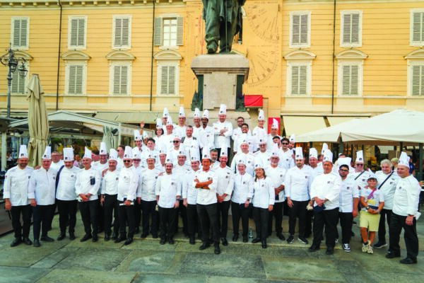 Gruppo di chef in divisa bianca posa per la Notte dei Maestri in piazza a Parma davanti al monumento di Giuseppe Verdi.