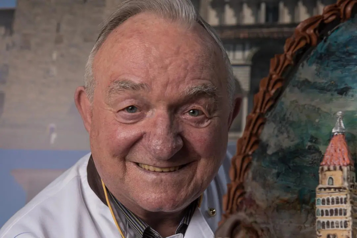 Ritratto del maestro pasticciere italiano Gastone Pegoraro sorridente accanto a una sua creazione artistica in zucchero.