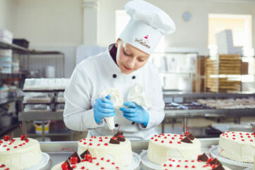 Pasticcera professionista decora torte vegane per il concorso Vegâteau 2026 in un laboratorio di pasticceria vegetale.