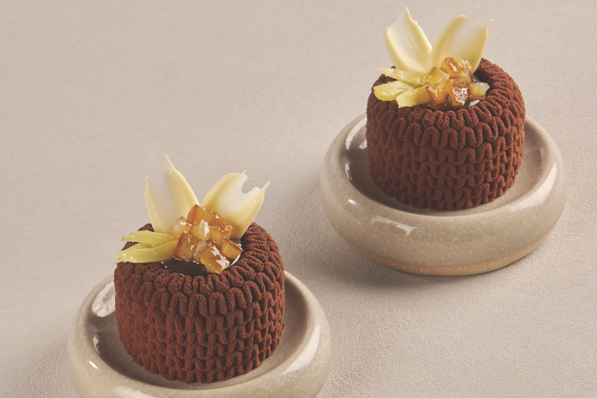 Due monoporzioni al cioccolato con decorazioni di zenzero candito e petali di cioccolato bianco su piattini in ceramica.