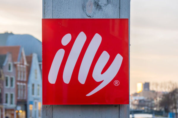 Insegna quadrata rossa con logo illycaffè su sfondo urbano, simbolo della crescita dei ricavi dell'azienda italiana.