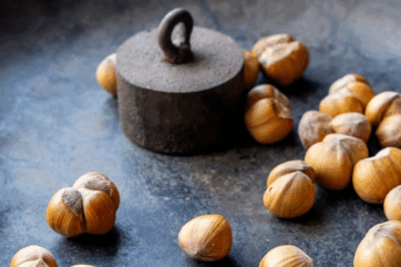 Nocciole IGP Agrimontana e Cascina Baronina: nocciole intere con guscio disposte accanto a un antico peso in ferro.