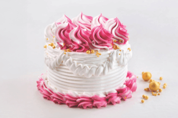Torta rosa e lamponi decorata con panna, ciuffi di crema sfumata, perle dorate e dettagli eleganti su sfondo bianco.