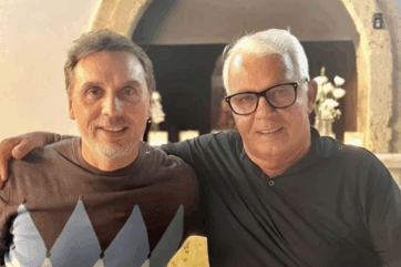 Due uomini sorridenti, un manager e un imprenditore, durante l'acquisizione Unigrà in un contesto professionale.