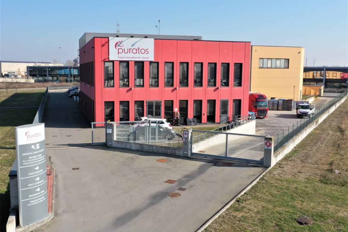 Facciata della sede Puratos a Parma con logo aziendale, uffici, parcheggio e camion in un'area industriale moderna.