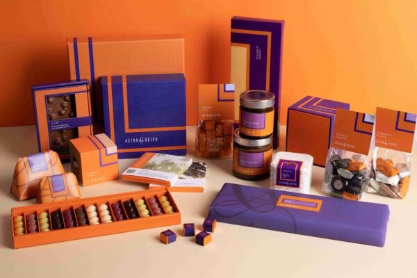 Collezione 26-27 Guido Gobino: elegante assortimento di praline, cremini e confezioni regalo blu e arancioni.