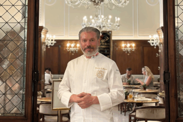 Domenico Di Clemente, chef in divisa bianca, posa all'interno di un elegante ristorante di lusso con lampadari classici.