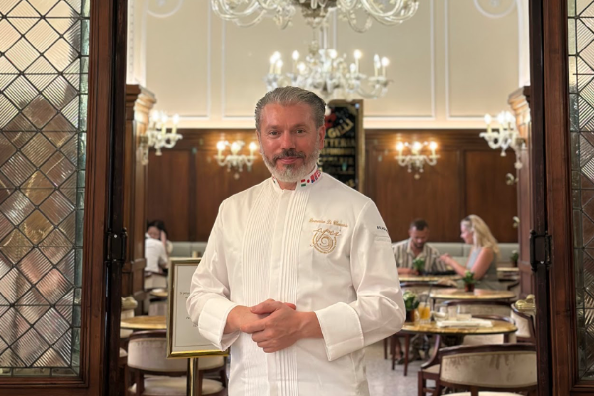 Domenico Di Clemente, chef in divisa bianca, posa all'interno di un elegante ristorante di lusso con lampadari classici.
