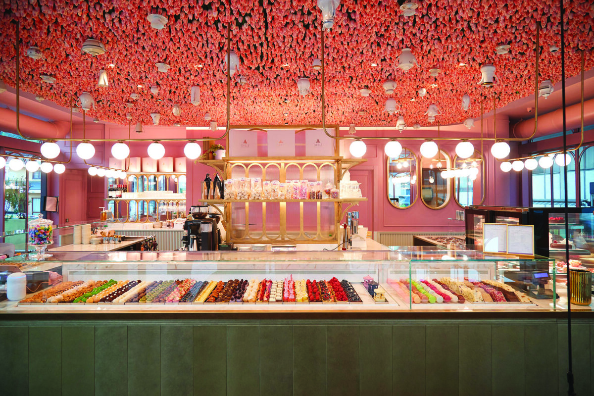 Interni della pasticceria Mignon Ofelè con bancone di pasticcini colorati e soffitto decorato con fiori rosa e tazze.