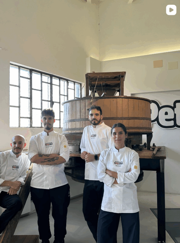Quattro chef in divisa bianca posano davanti a una grande macina in legno, pronti per la finale