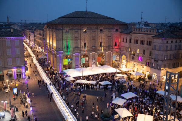 Veduta aerea della Cena dei Mille in piazza Garibaldi a Parma con tavolata infinita e illuminazione tricolore serale.