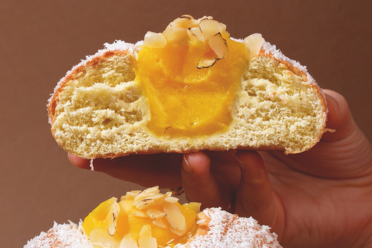 Perla Veneziana: soffice brioche farcita con crema gialla, scaglie di mandorle e granella di cocco in mano.