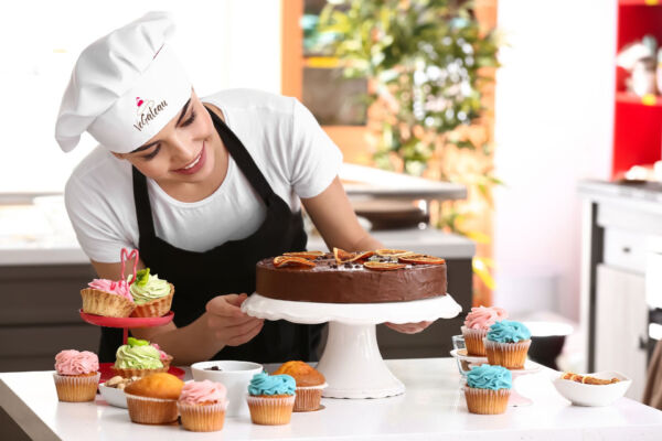Pasticcera sorridente decora torta al cioccolato e cupcake colorati in cucina professionale