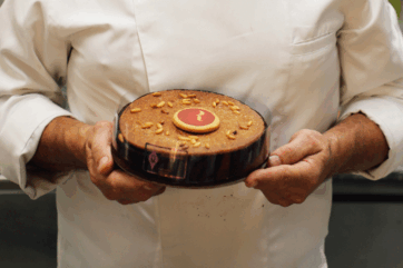 Chef presenta la torta Respighiana, omaggio di dolcezza con granella di nocciole e disco di cioccolato.