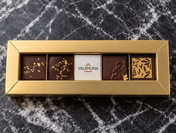 Scatola regalo in oro Valrhona con 5 cioccolatini Guanaja 70%, inclusa tavoletta con logo, su marmo nero.