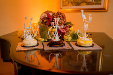 Dessert Couture di Giuseppe Manilia: tre dolci artistici in passerella con decorazioni floreali bianche su tavolo lucido