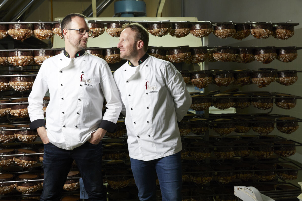 Andrea e Lorenzo Filippi in divisa da pasticceri sorridono davanti a scaffali di dolci. 10 anni B Corp.