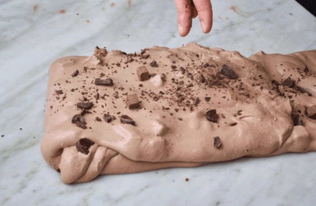 Impasto al cioccolato steso su marmo con scaglie e cubetti, mano che aggiunge ingredienti per ricette