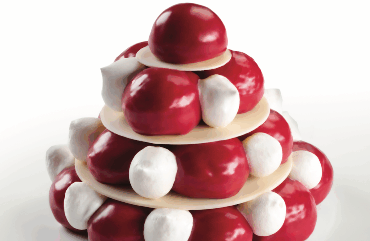 Torre di profiterole Frambolles con sfere rosse lucide e ciuffi di panna bianca su vassoi rotondi