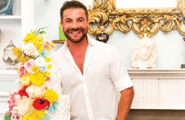 Renato Ardovino sorridente accanto a una torta floreale colorata, pasticceria d'arte in ambiente elegante.