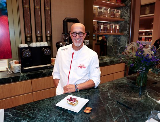 Chef sorridente in divisa bianca dietro il bancone in marmo di una bakery con macchina Nespresso e dolce.