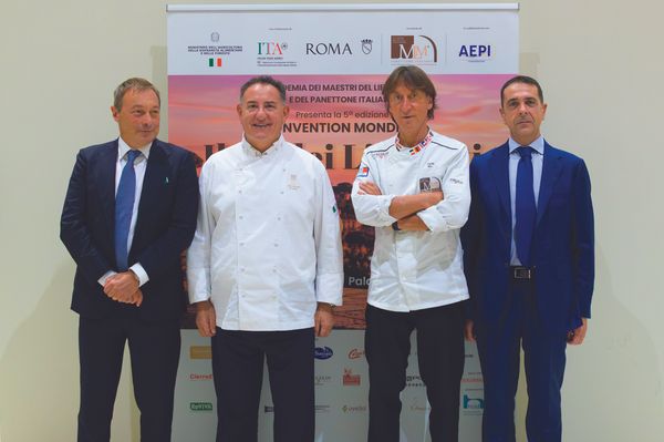 Quattro uomini in abiti formali e da chef posano davanti al Manifesto del Panettone italiano, tra filiera e innovazione.