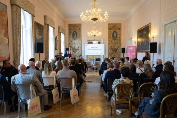 Pubblico seduto in una sala elegante con lampadario e schermo per conferenza e presentazione aziendale