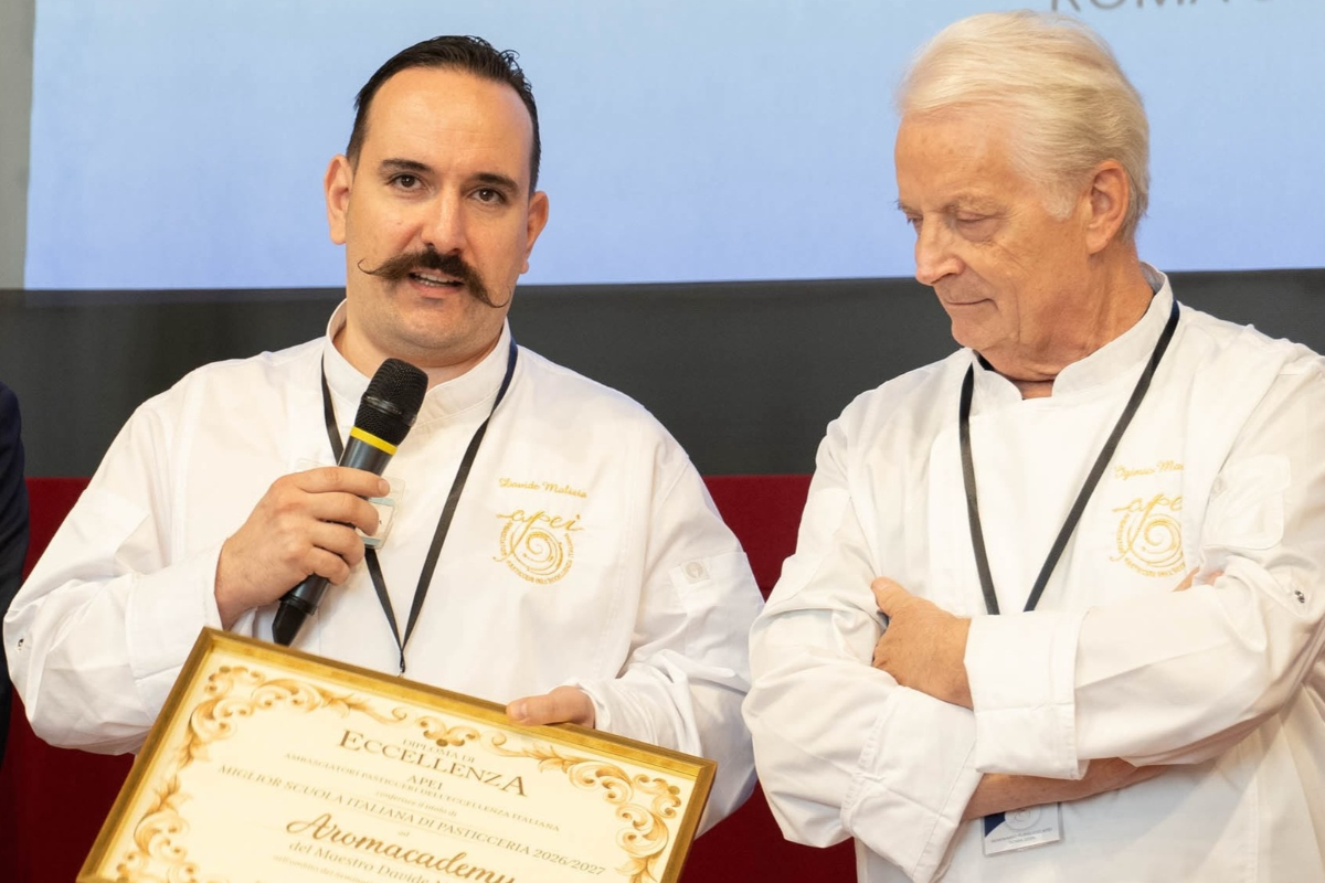 Chef Davide Malizia con giacca bianca e microfono tiene una pergamena durante una cerimonia di premiazione