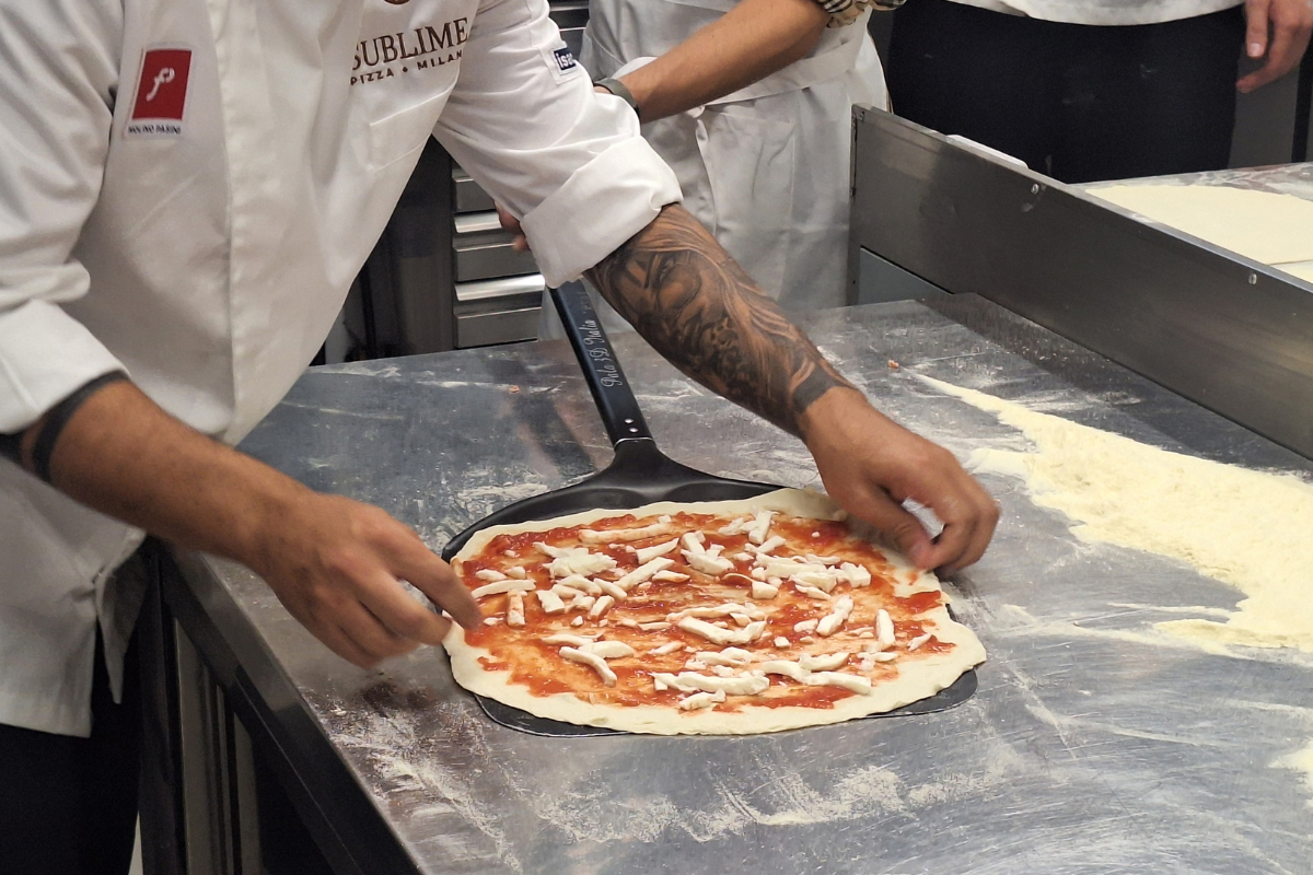 Pizzaiolo stende pizza milanese contemporanea con Molino Pasini, farina e mozzarella in cucina.