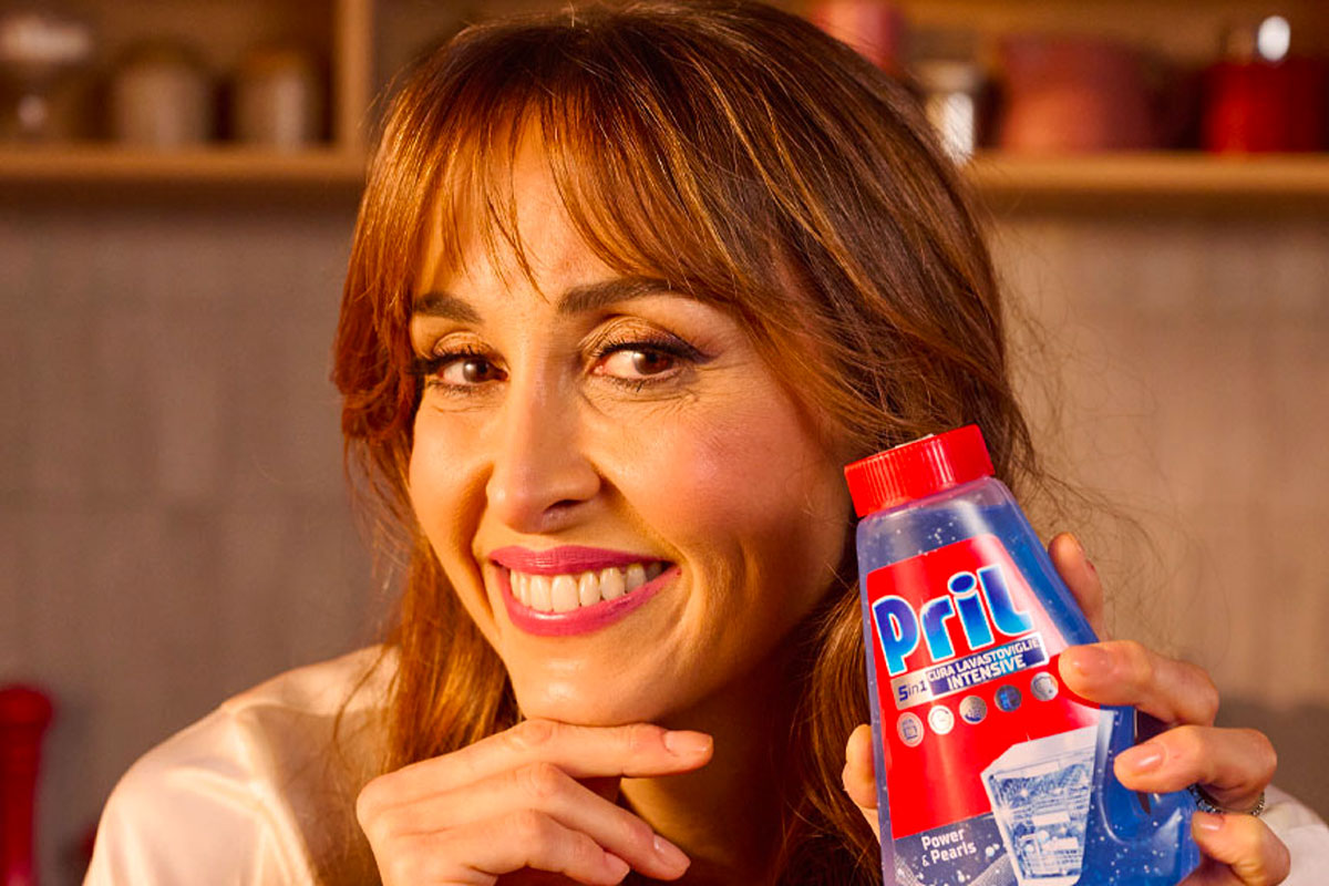 Donna sorridente mostra Pril Cura Lavastoviglie Intensive 5in1. Pulizia e cura lavastoviglie.