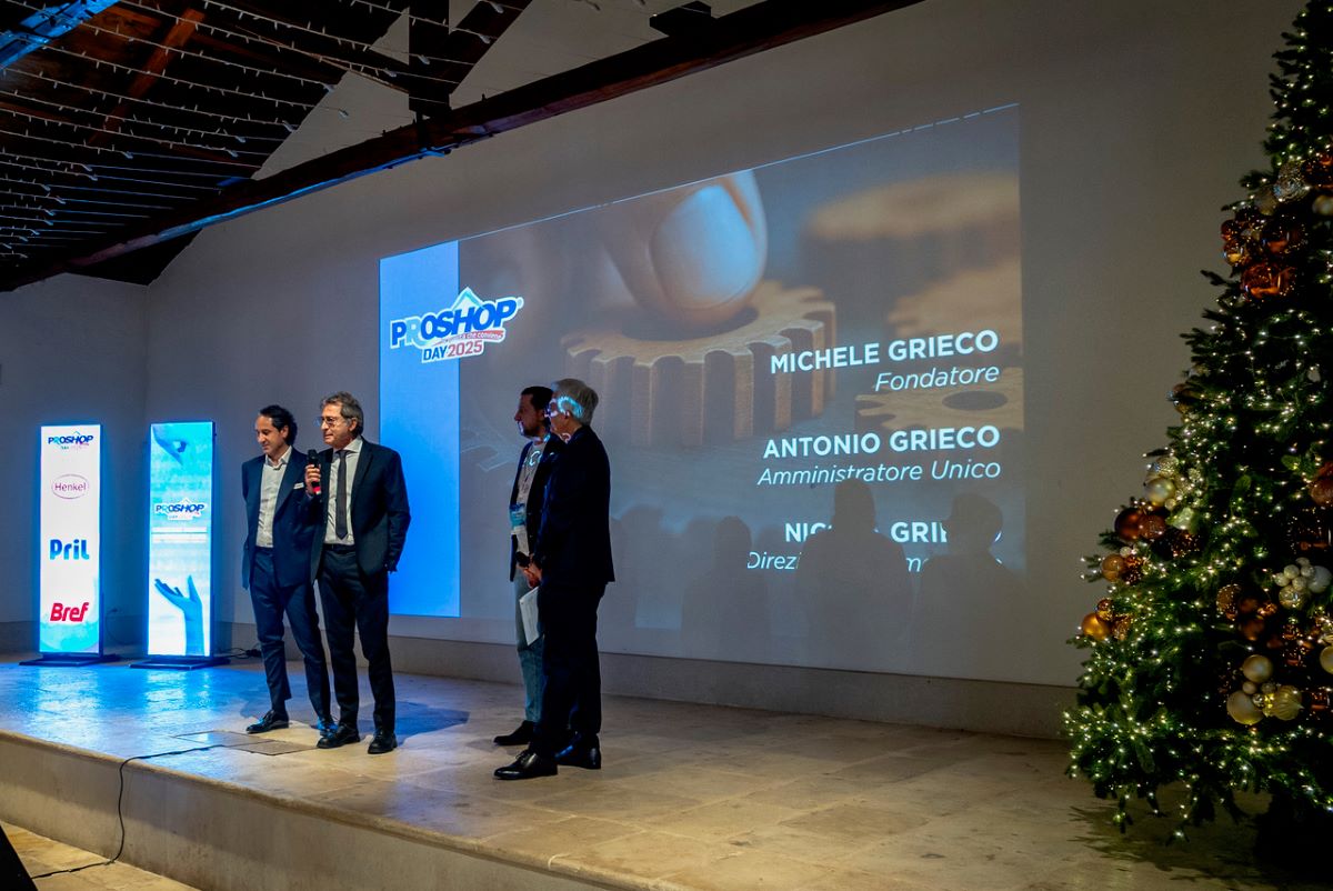 Evento Proshop Day 2025: relatori sul palco, albero di Natale. Presentazione aziendale e networking.