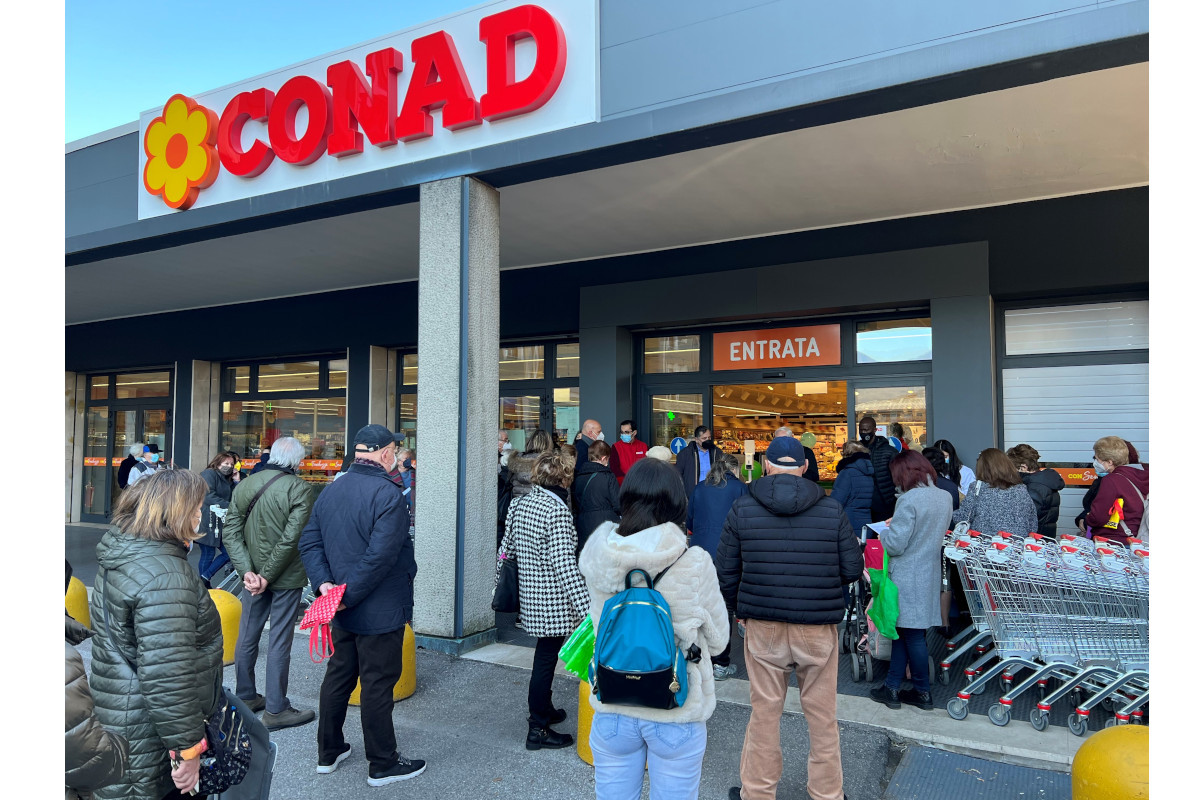 Esterno del Conad di Brescia, via Vivanti. Persone in fila all'entrata del supermercato. Carrelli della spesa.