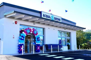 Negozio Acqua & Sapone. Facciata bianca con arco di palloncini colorati all'ingresso. Carrelli spesa in fila.