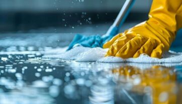 Mano con guanto giallo pulisce il pavimento con mocio e detersivo per la cura della casa e igiene professionale.