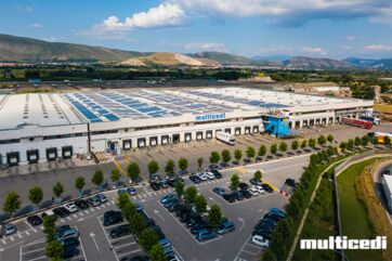 Veduta aerea del polo logistico Multicedi con magazzini, parcheggio e camion, simbolo del fatturato record 2025.