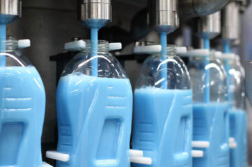Linea di produzione Henkel: riempimento automatico di flaconi in plastica con detergente blu per l'home care.